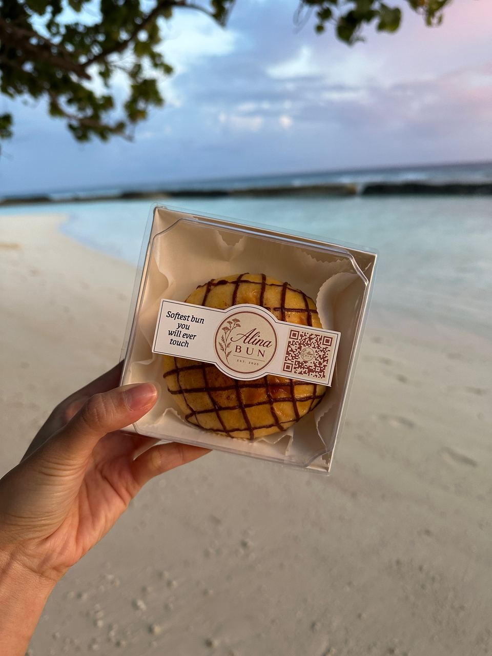 A boxed chocolate bun on the beach, with the sea behind