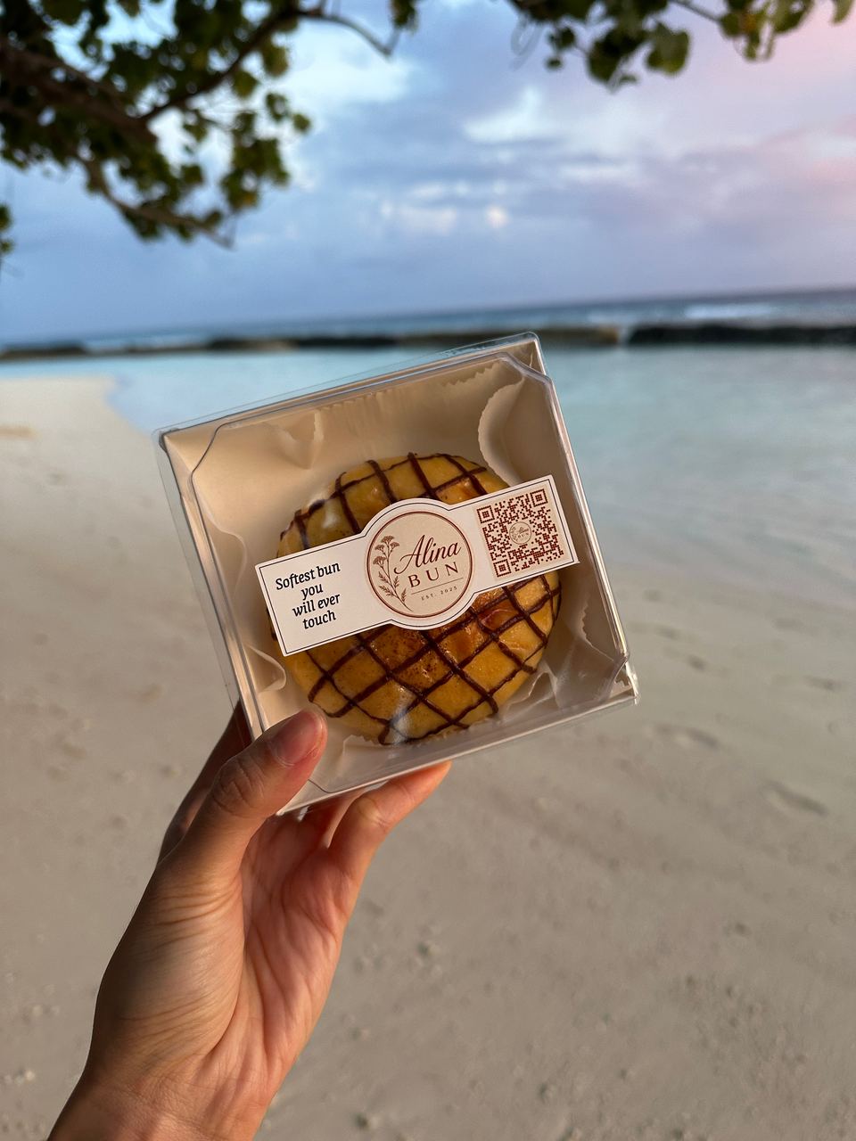 A boxed chocolate bun held up on a Maldives beach