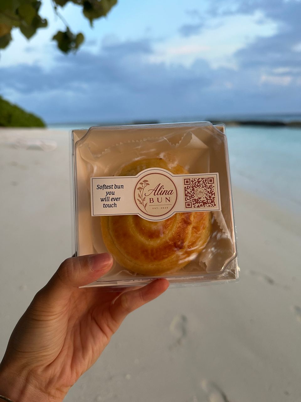 A boxed cream bun held up on the beach in the evening