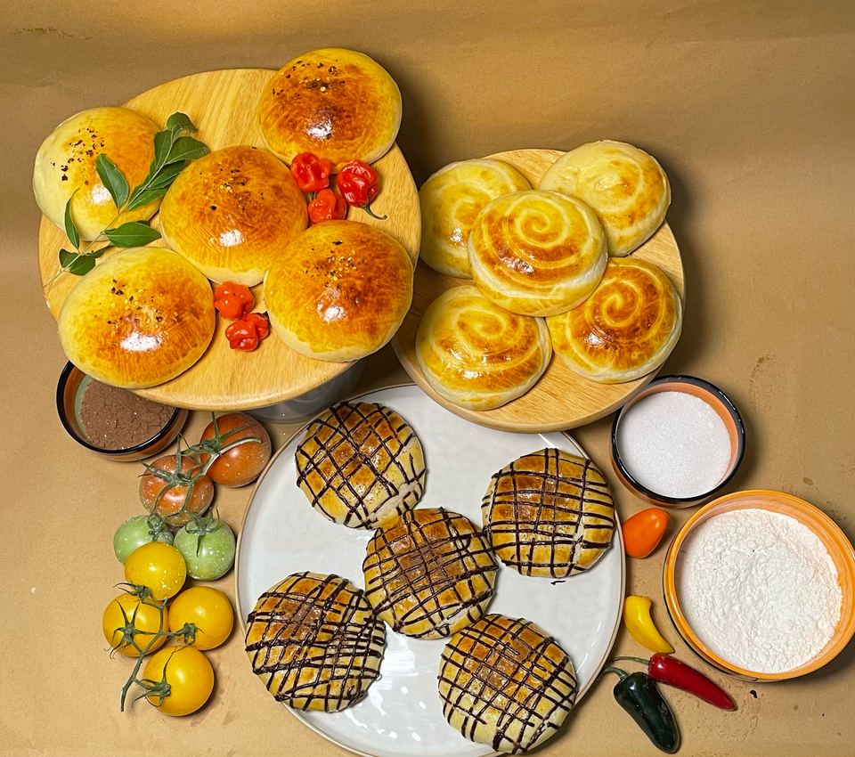 Tuna, cream and chocolate buns on wooden boards and a plate, with tomatoes, chillies, flour and sugar on kraft paper