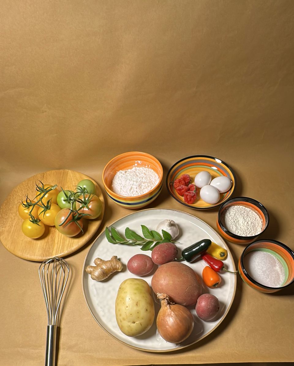 Ingredients laid out on kraft paper: flour, sugar, eggs, tomatoes, potatoes, onions, ginger, chillies and curry leaves