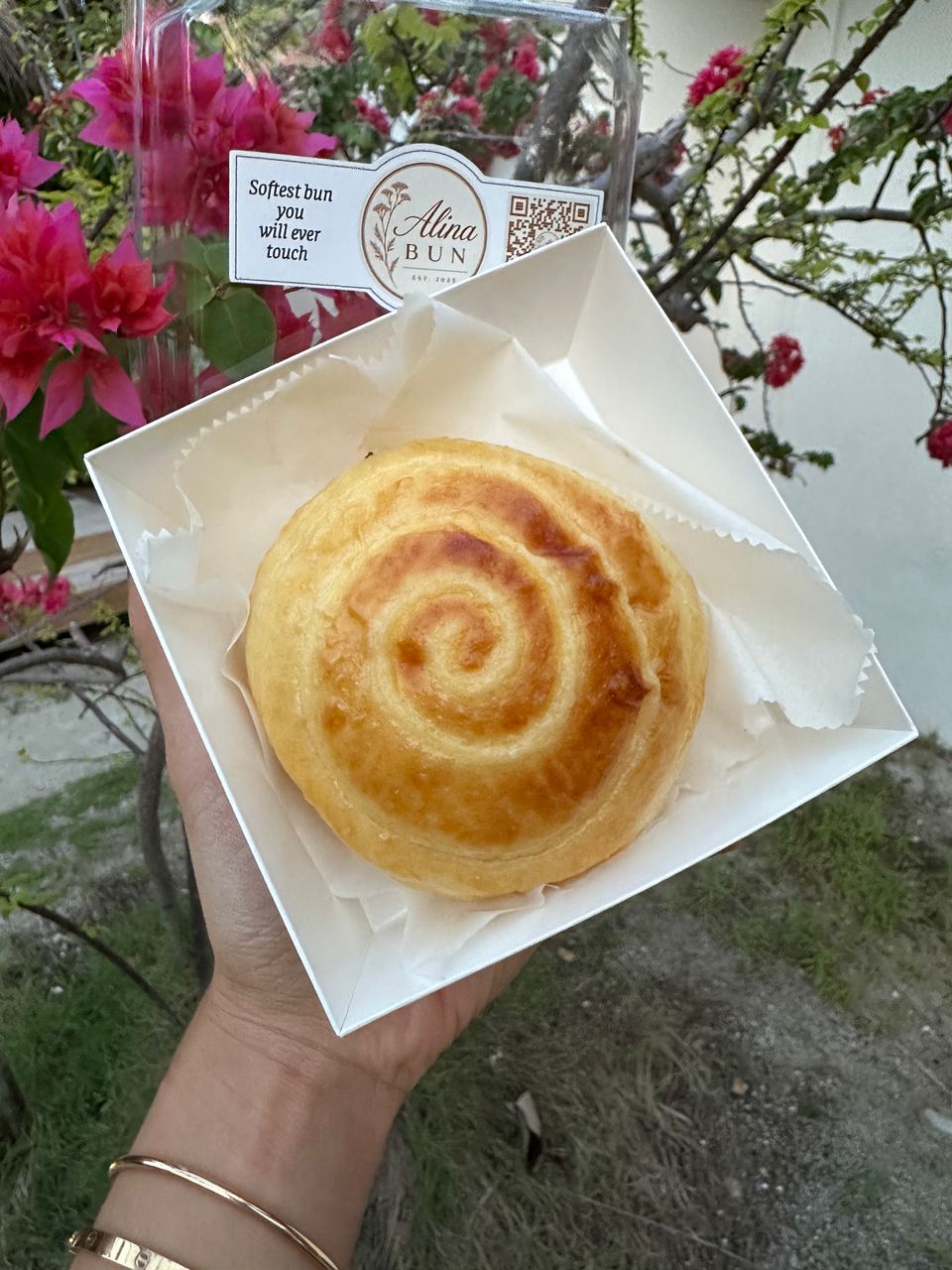 A cream bun in its box among pink bougainvillea