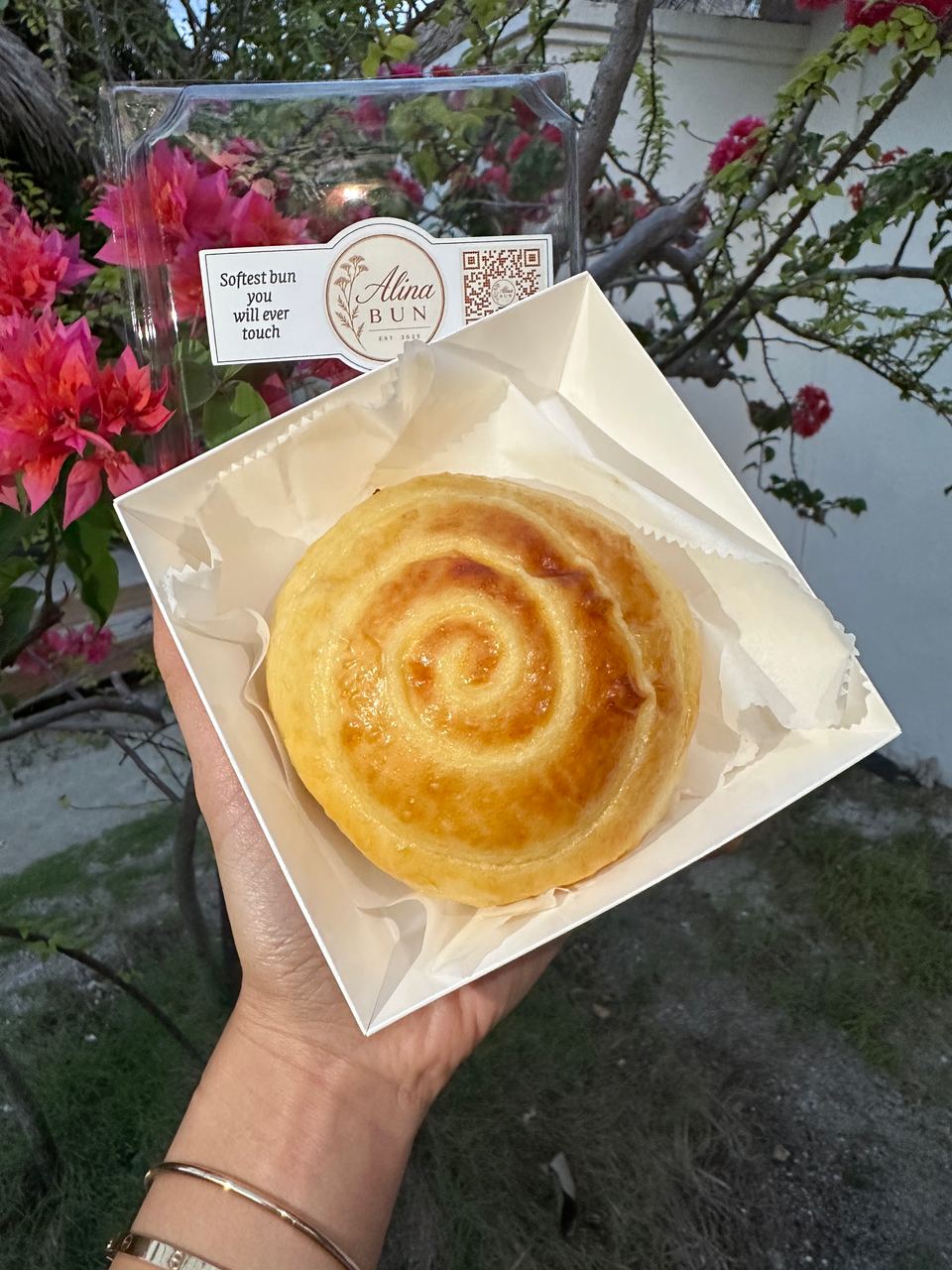A cream bun held up in front of bougainvillea